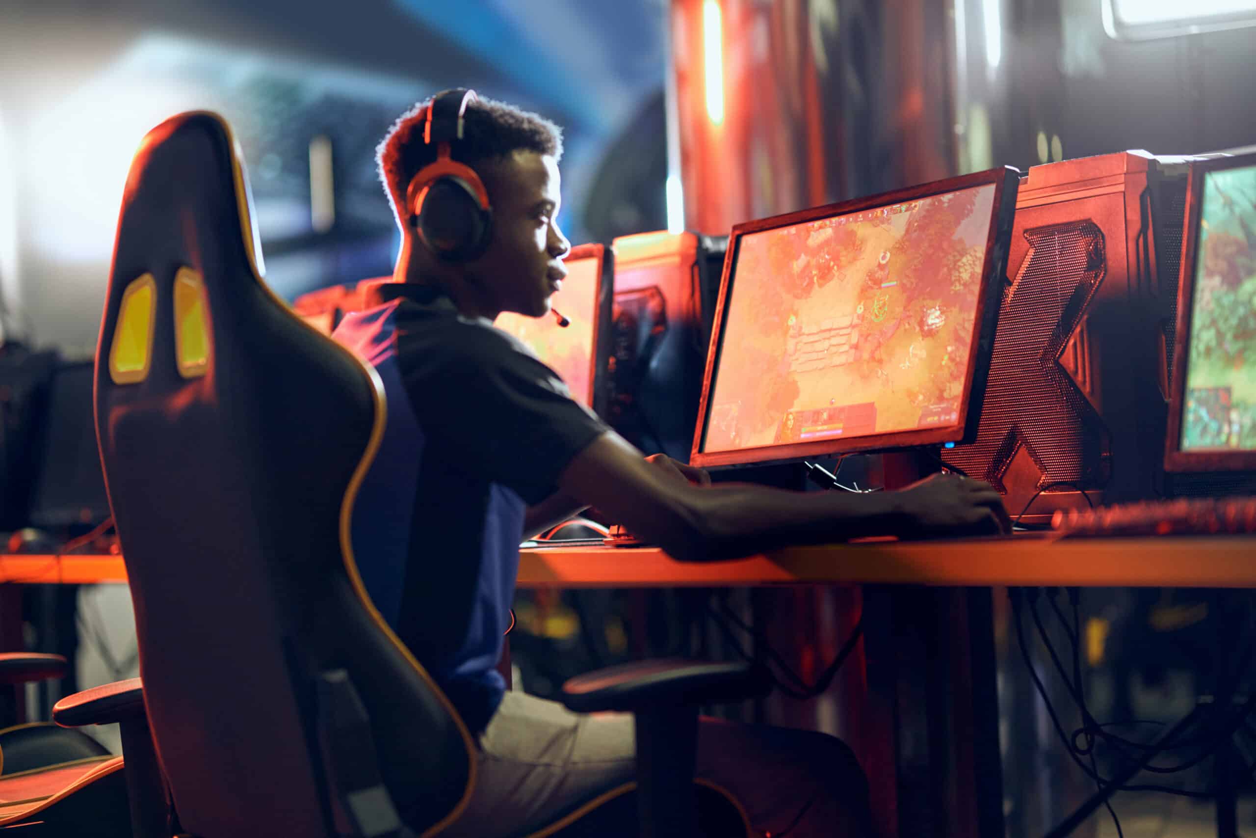 Gamer in headphones and dark shirt, focused on a glowing screen amidst dimly lit gaming gear.