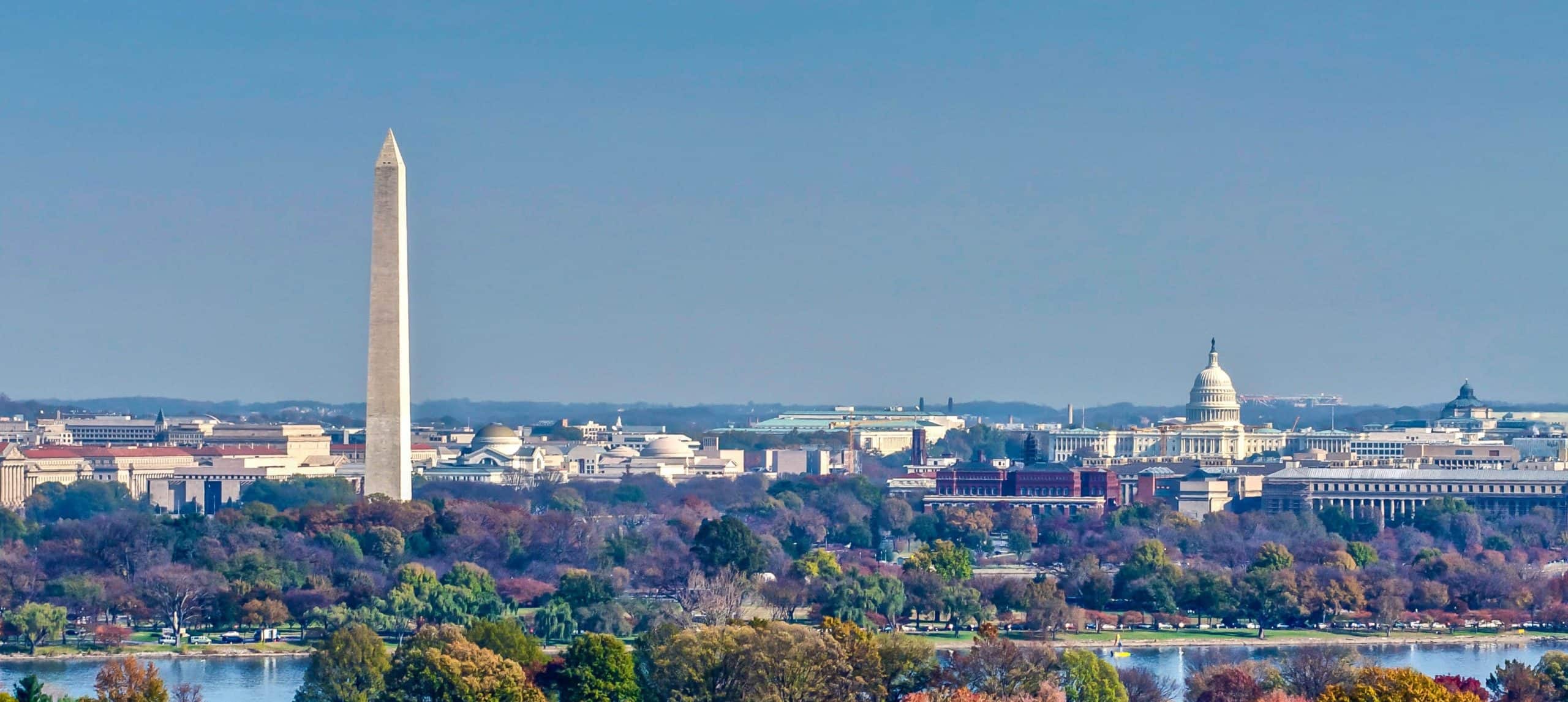 Washington D.C. aerial: Washington Monument left, U.S. Capitol right, autumn trees, Potomac River in front.