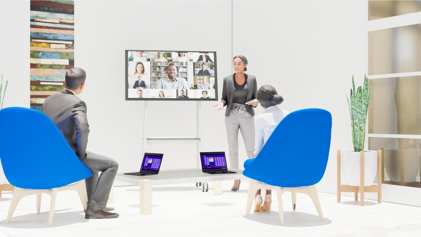 Woman speaks to colleagues in a modern meeting room with blue chairs, a plant, and two laptops.
