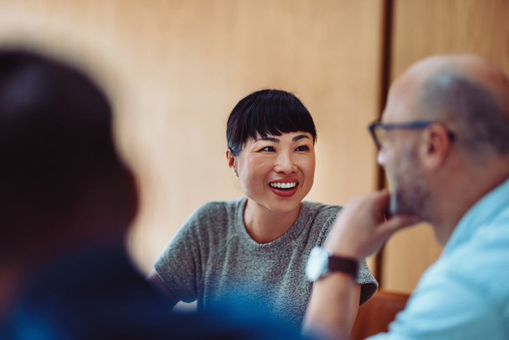 Close up of smiling woman in a hybrid meeting with two coworkers